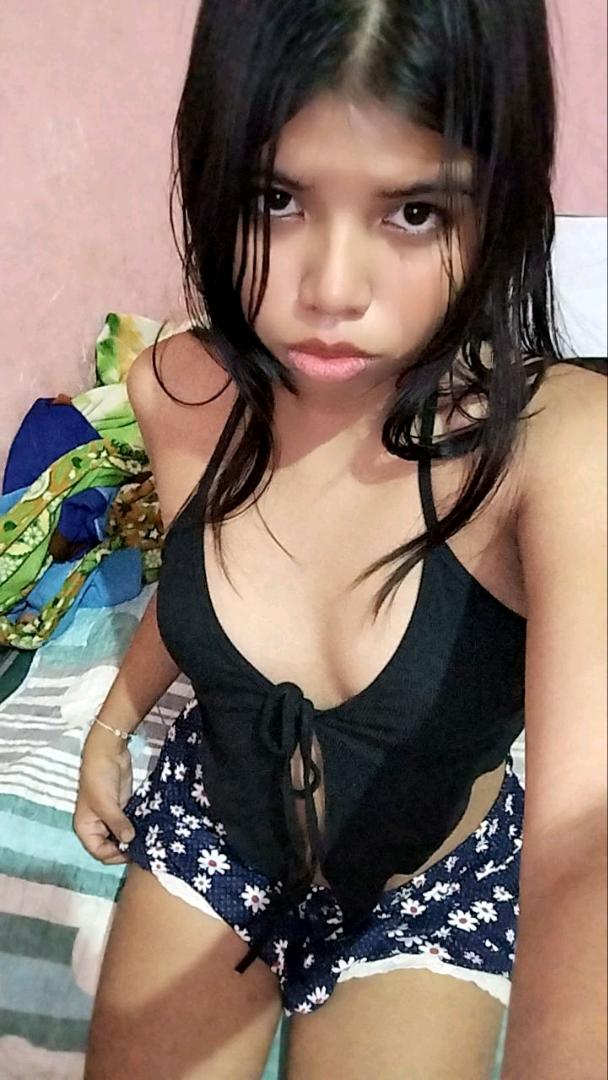 A young woman in a black tie-front top sitting on a bed in moody light