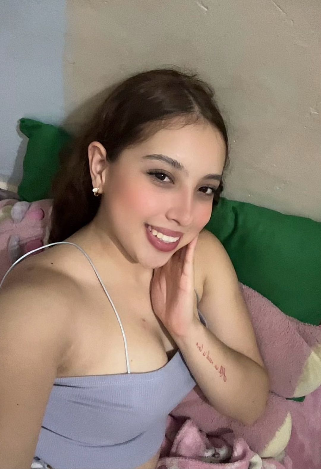 Encantadora, CO — latina, brown ponytail, vertical half-body, lavender cami on bed, big warm smile, hand on 